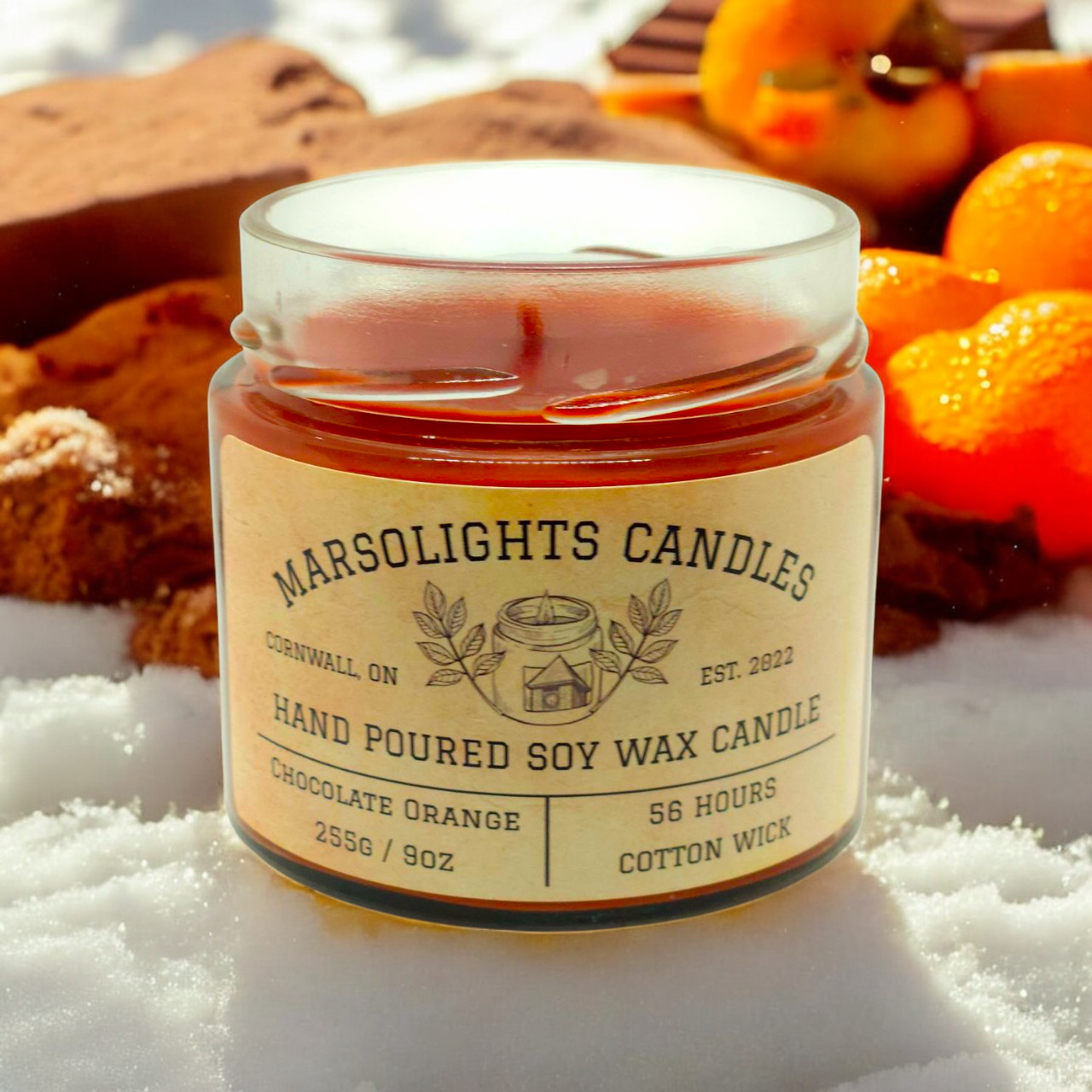 Chocolate Orange Scent Soy Candle on top of snow with chocolate and oranges in the background.