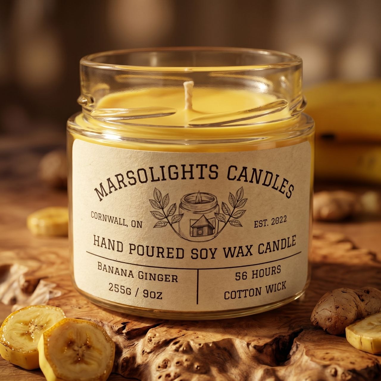 A glass jar candle with a cream label reading Marsolights Candles, Banana Ginger, 56 hours, 2556 / 9 oz, set on a rustic wooden surface with sliced bananas and ginger pieces around it.