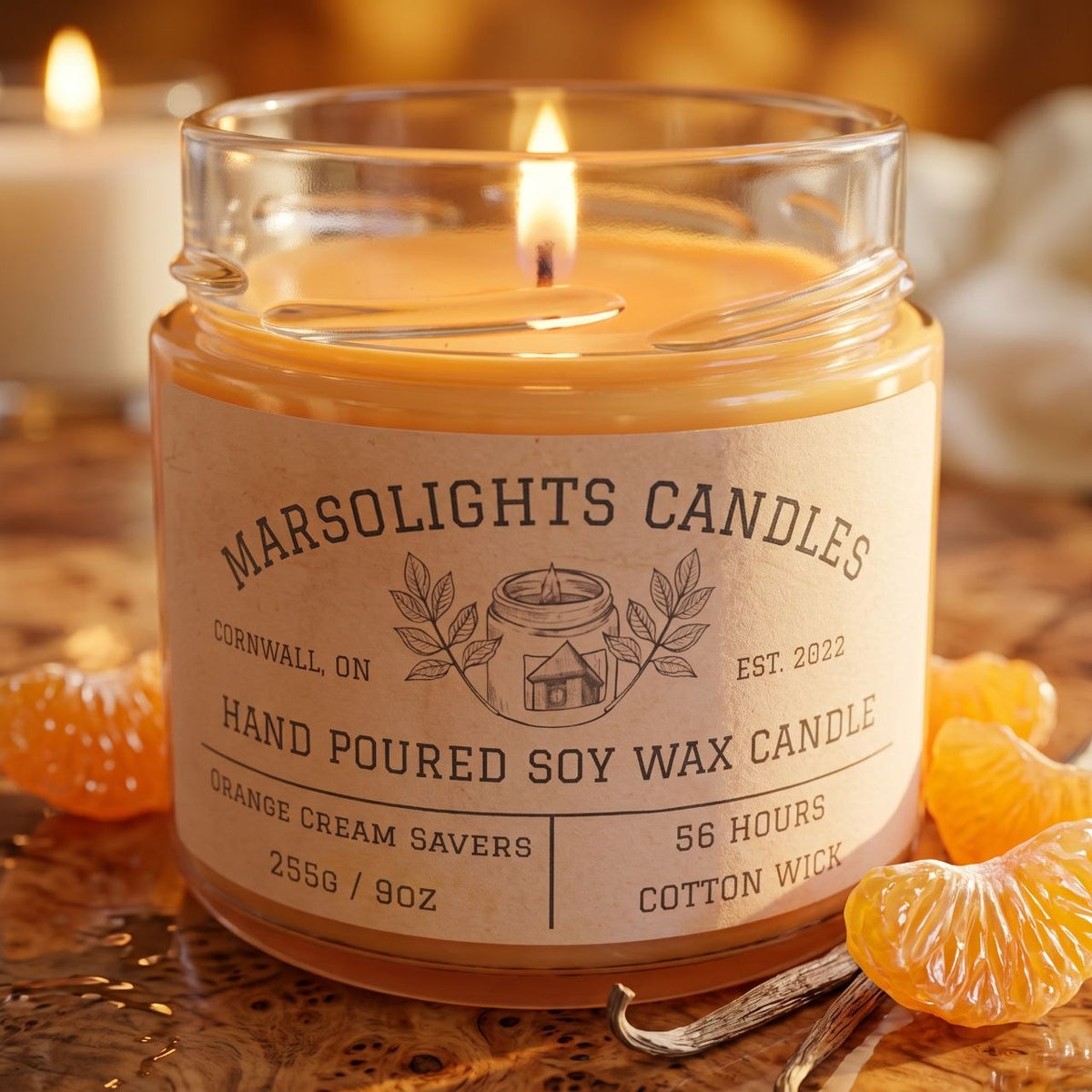 Orange Creme Saver Soy Candle on a table with warm, inviting décor. Our candle features sweet citrus, creamy vanilla, soft buttery tones and a sweet citrus infusion. 9 ounce or 255 grams, 56-hour burn time, cotton wick, soy candle, made in Canada, paraben free.