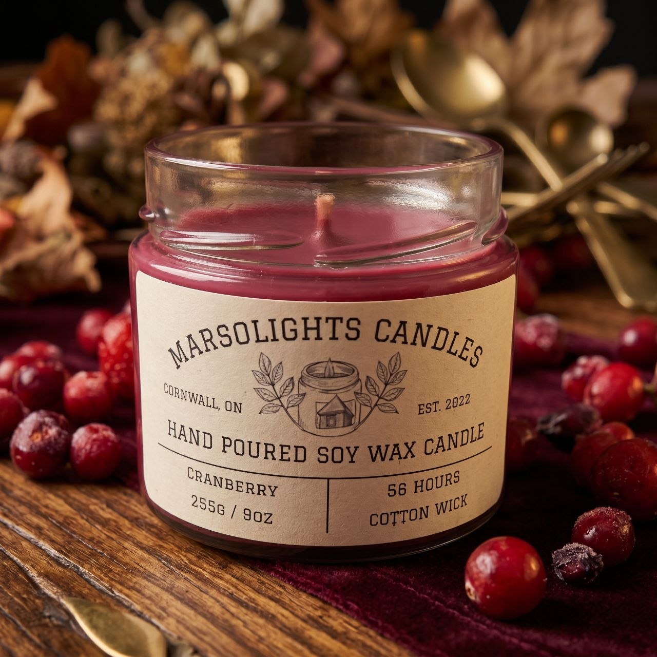 Soy Cranberry Scented Candle on Wooden Table with Cranberry and other  fall themed decor. Candle Size is 9 ounce or 255 grams. Cotton Wick, Soy Candle with a 56 hour estimated burn time. Candle Features notes of Cranberries, Ripe Berries, and a finishing base with Tonka Bean notes. 