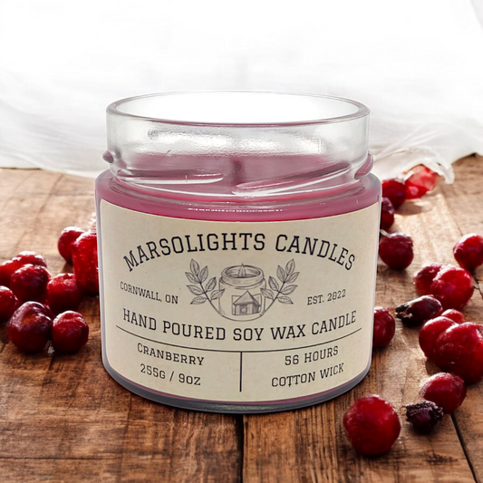 A Red Cranberry Candle on a Wooden table with fresh cranberries with a light mist of water on them. Scented with a Tonka Base, Wild Berry Vines, and finally with a tantalizing Cranberry aroma. 