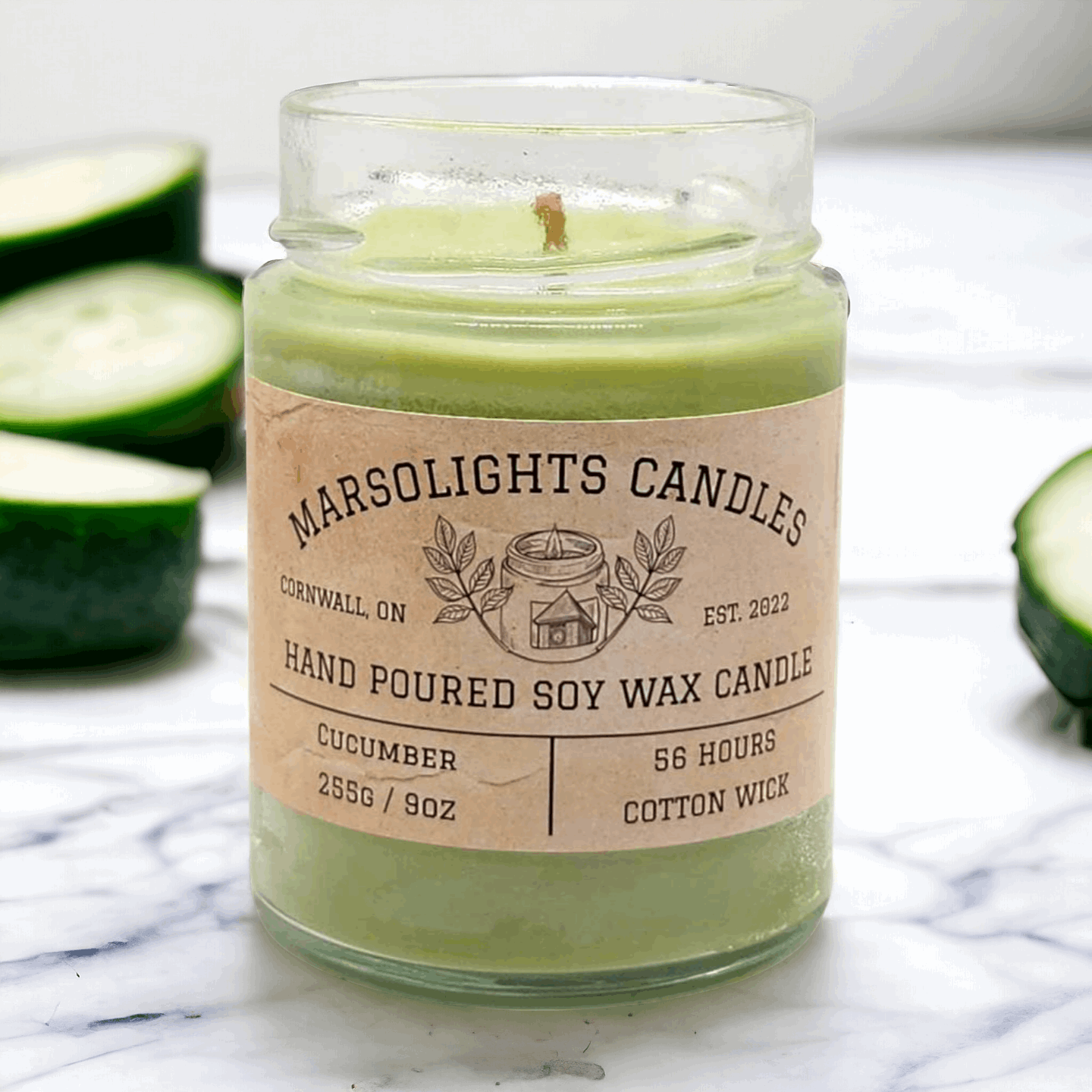 9 ounce green cucumber scented soy candle in a glass library jar on top of a counter with fresh cucumber slice around it and in the background