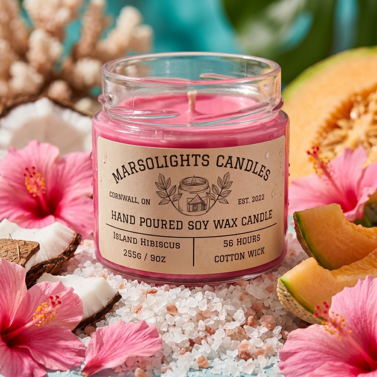 Island Hibiscus Scented Soy Candle Made in Canada Sitting on Sand and Salt Petal with Pink Hibiscus, fresh melon, and coconut surrounding it. This candle is 9 ounce or 255 grams, has an estimated burn time of 56 hour with a cotton wick is made in Cornwall Ontario. $20 CAD