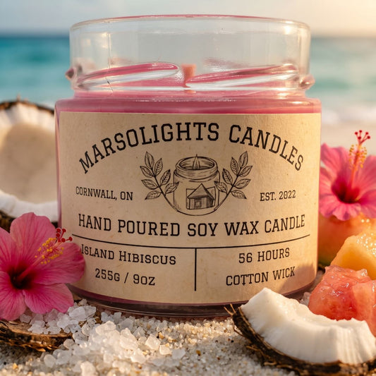 Island Hibiscus Scented Soy Candle Made in Canada Sitting on Sand and Salt Petal with Pink Hibiscus, fresh melon, and coconut surrounding it. This candle is 9 ounce or 255 grams, has an estimated burn time of 56 hour with a cotton wick is made in Cornwall Ontario. $20 CAD