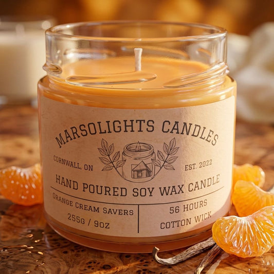 Orange Creme Saver Soy Candle on a table with warm, inviting décor. Our candle features sweet citrus, creamy vanilla, soft buttery tones and a sweet citrus infusion. 9 ounce or 255 grams, 56-hour burn time, cotton wick, soy candle, made in Canada, paraben free.