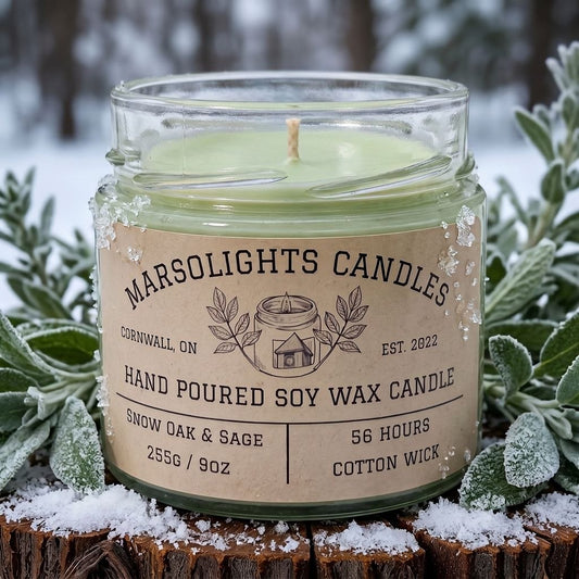 Snow Oak & Sage Soy Candle displayed with winter-inspired décor. The candle features clary sage, bergamot and snow-filled air, with frosted lavender, fir needle and black tea leaves, finished with cedarwood, soft grey wool and white oak. 9 ounce or 255 grams, 56-hour burn time, cotton wick, soy candle, made in Canada, phthalate free.