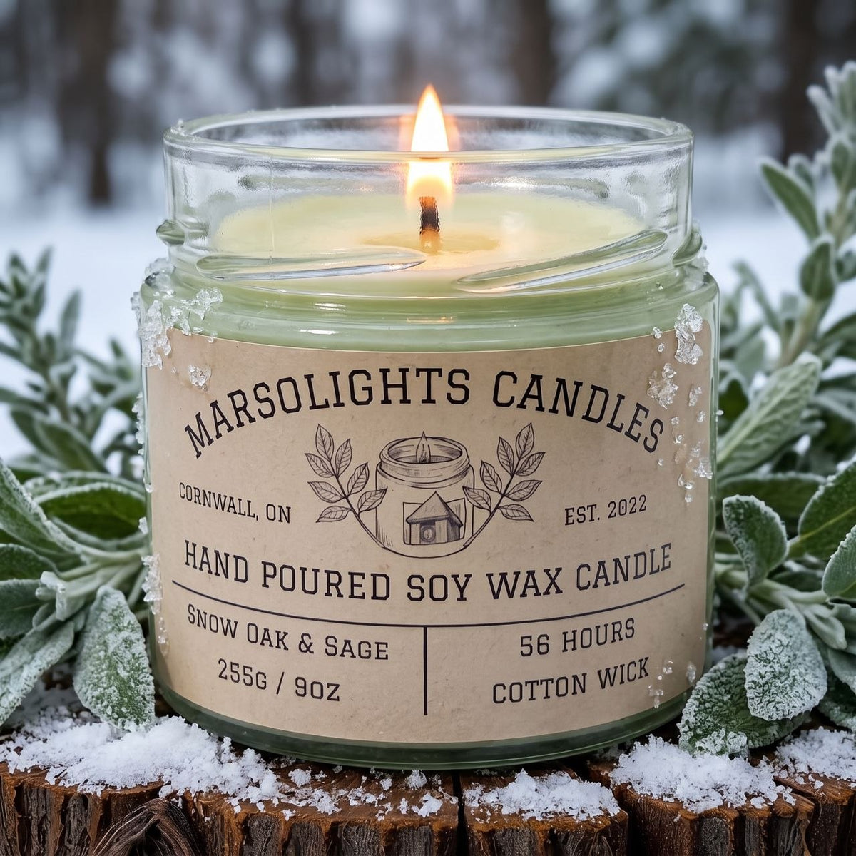 Snow Oak & Sage Soy Candle displayed with winter-inspired décor. The candle features clary sage, bergamot and snow-filled air, with frosted lavender, fir needle and black tea leaves, finished with cedarwood, soft grey wool and white oak. 9 ounce or 255 grams, 56-hour burn time, cotton wick, soy candle, made in Canada, phthalate free.